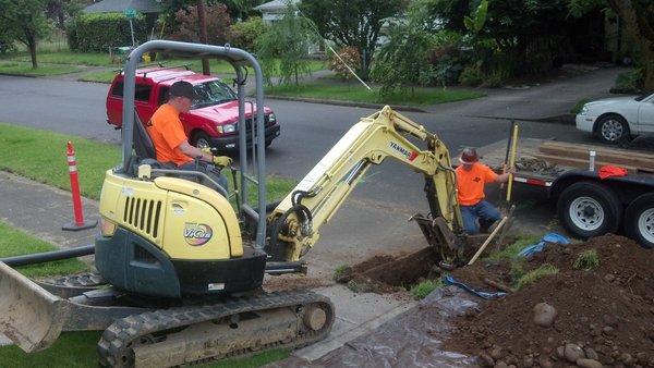 Excavator digging trench for construction at a residential site.